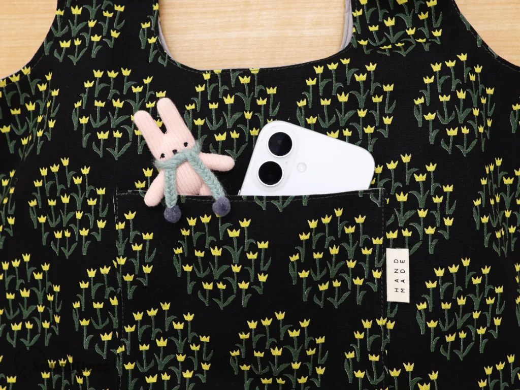 A white smartphone and a small plush charm inside the handy front outer pocket of the black patterned shoulder bag.
