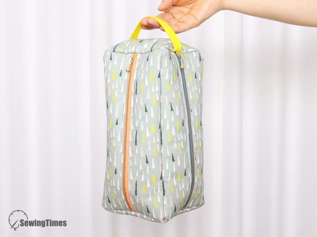 A person holding a handmade sage green quad-organizer pouch by its vibrant yellow top handle, showcasing its tall boxy shape and vertical zippers.