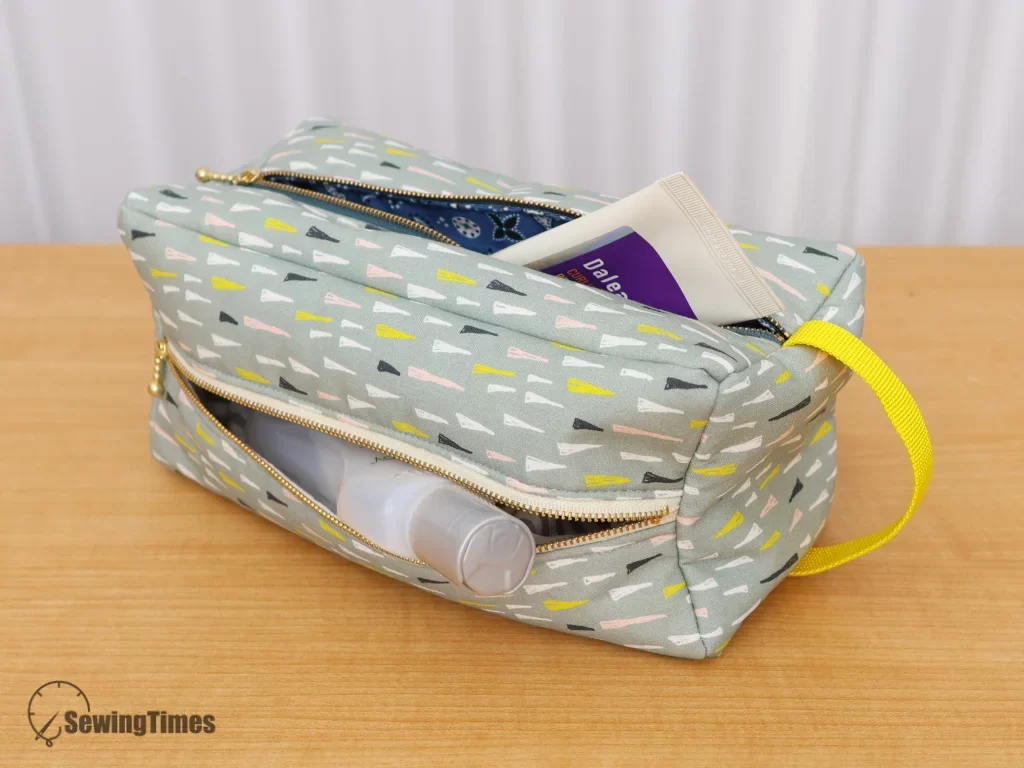 Close-up of a DIY 4-pocket travel pouch lying horizontally, with side zippers partially open to reveal skincare products inside separate compartments.