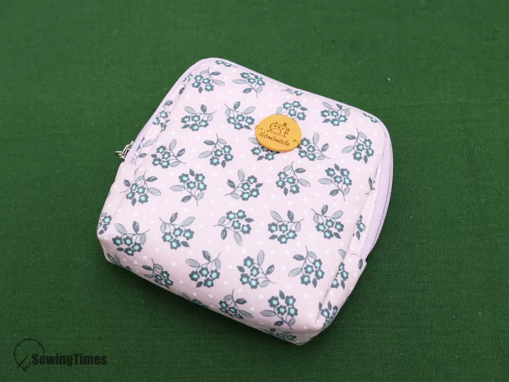 A completed handmade compact divided pouch with a pink floral pattern and zipper, standing upright on a green background.