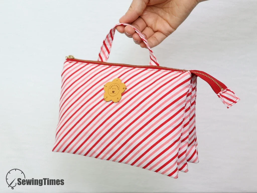 Hand holding a red and white striped 5-pocket pouch with handle and double zippers