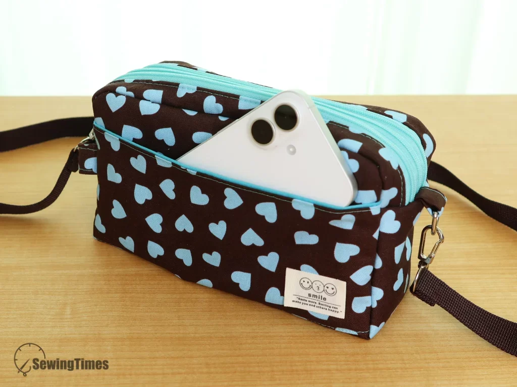 A white smartphone being tucked into the convenient front pocket of the Triple-Zip Crossbody Bag.