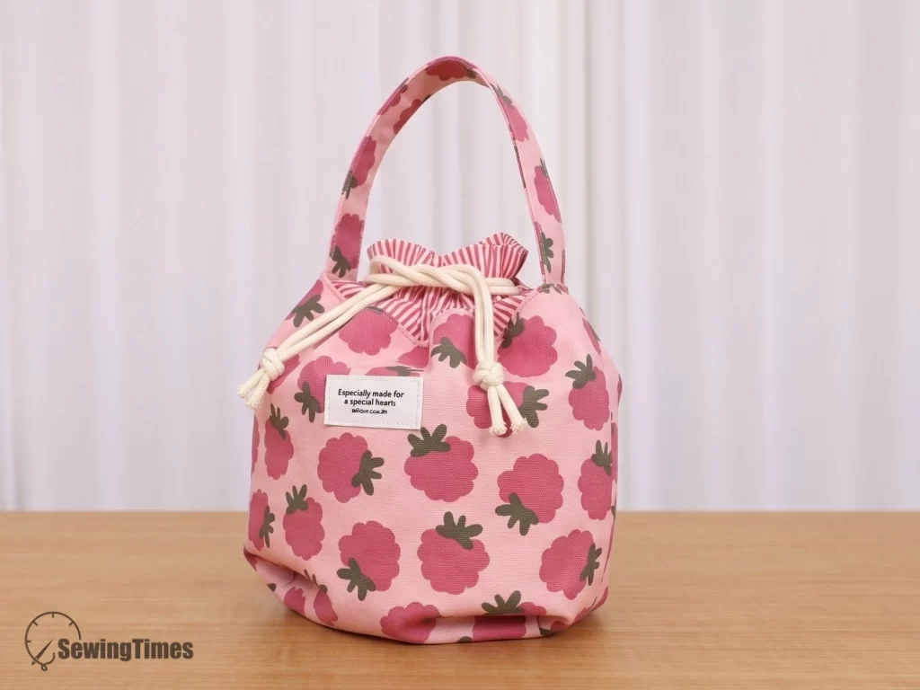 Pink drawstring bag with a dark pink raspberry pattern and white cords.