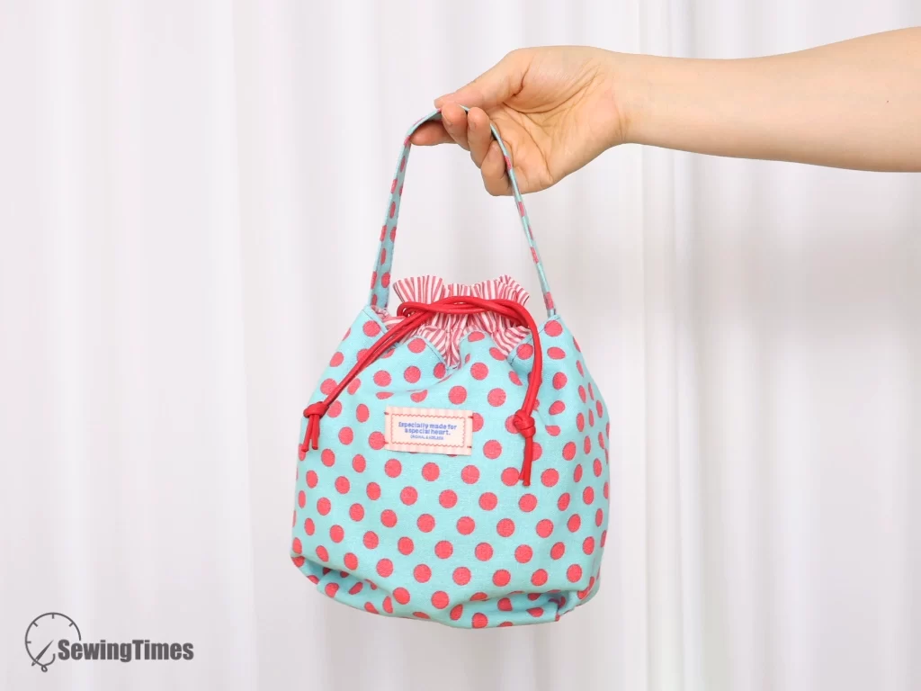 A hand holding a handmade light blue and pink polka dot drawstring pouch.