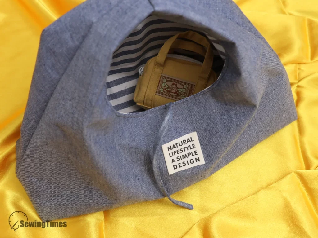 The interior view of a denim triangle bag showing a striped fabric lining and a white smartphone inside to demonstrate its storage capacity.