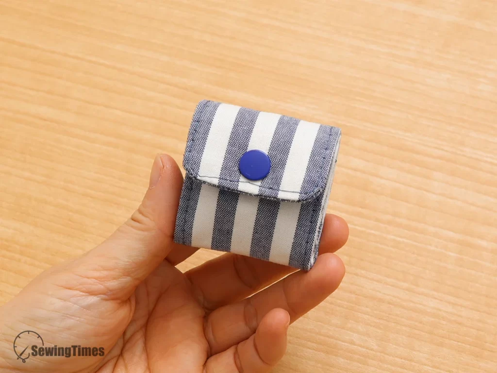 A small, compact blue and white striped trinket folder held in a hand to demonstrate its portable size for travel.