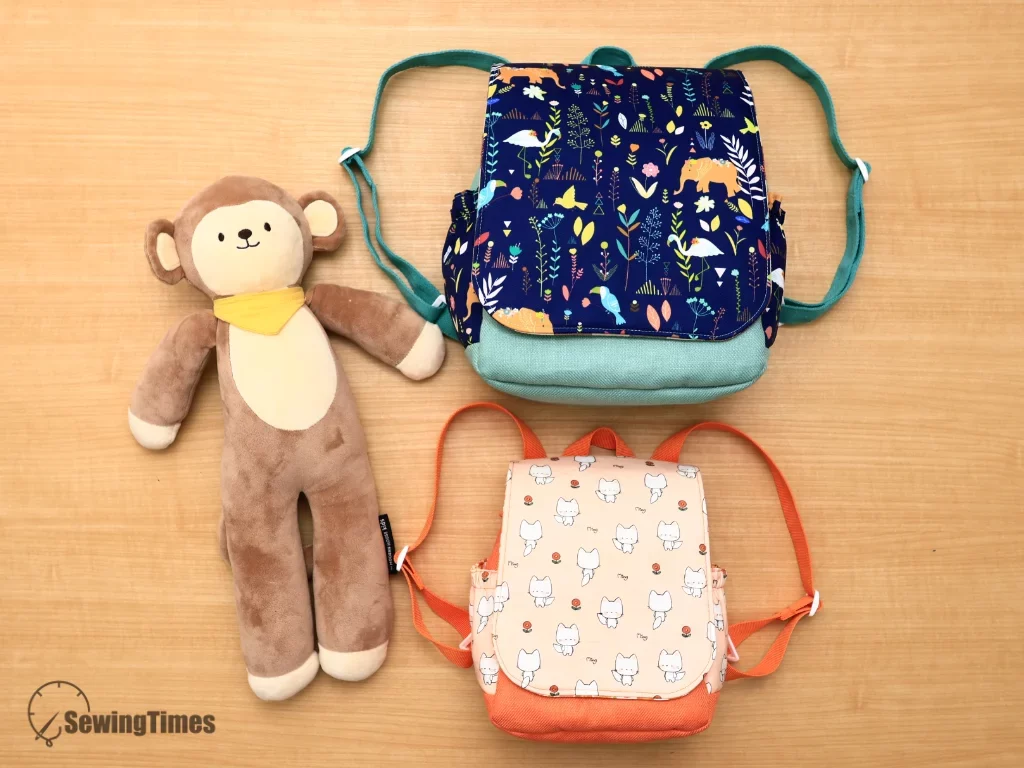 Top view flat lay featuring small peach and large navy Pebble kids backpacks with plush stuffed monkey.
