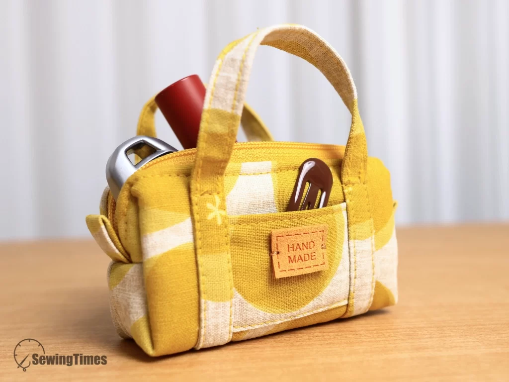 Yellow mini duffle pouch showing lipstick and small items inside the front pocket and main compartment.