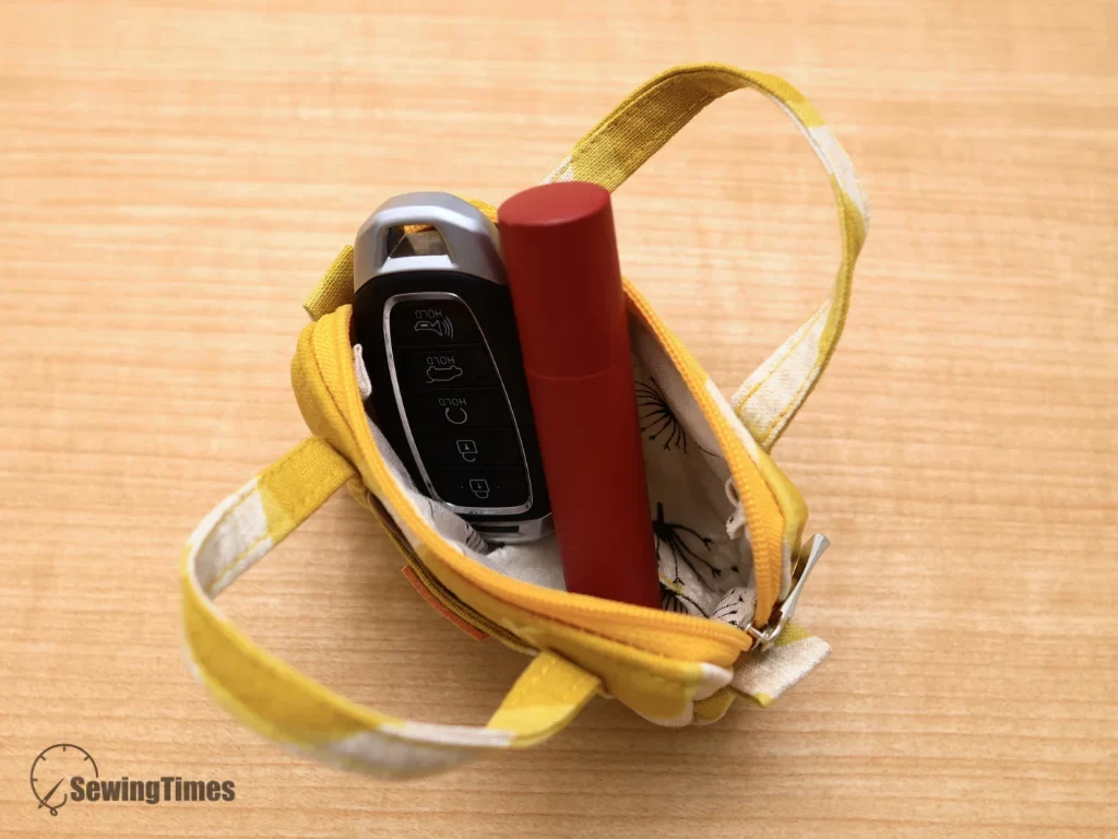 Top-down view inside a tiny yellow duffle pouch holding a car key fob and lip balm.