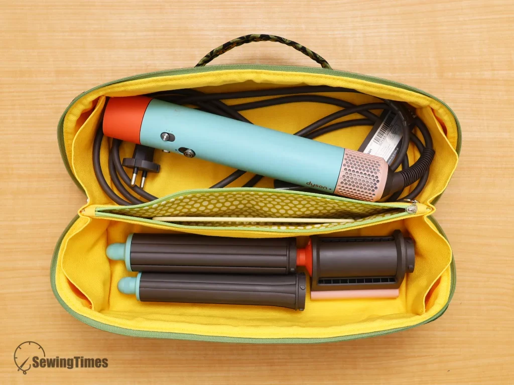 Interior view of an organized fabric pouch containing a hair styler, barrels, and brushes in dedicated compartments.