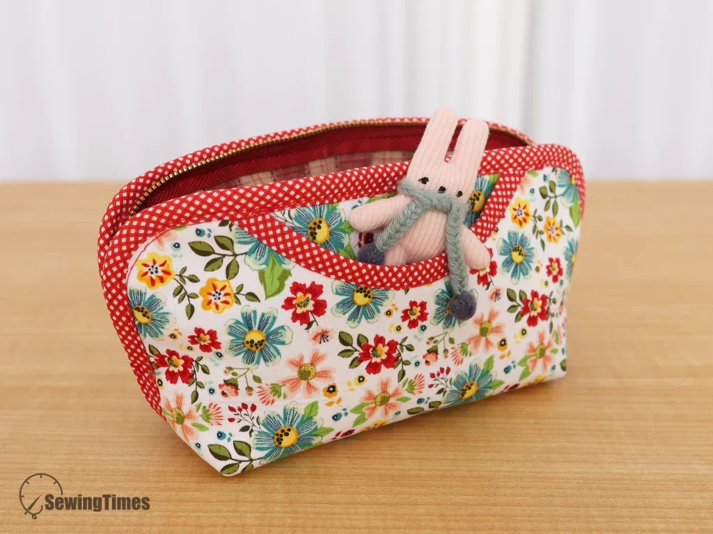 A small plush rabbit toy tucked into the curved front outer pocket of the floral fabric pencil case, demonstrating extra storage.