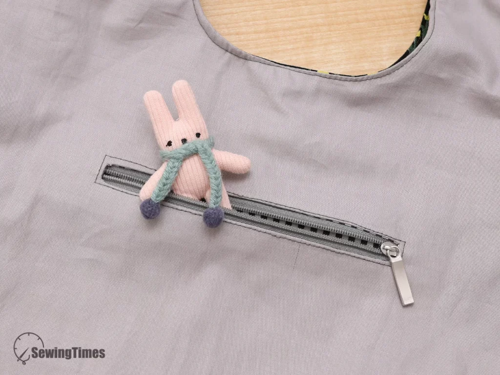 Close-up of a secure gray inner zipper pocket lined inside the DIY shoulder bag with a small pink plush bunny accessory peeking out.