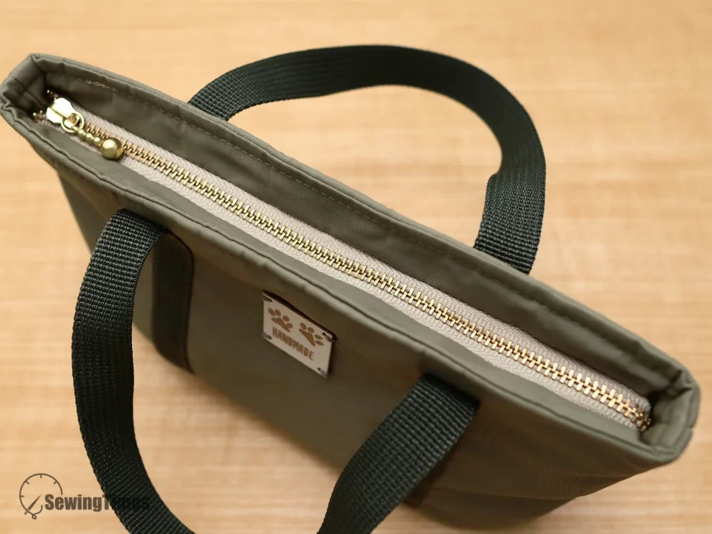 Close-up of the neat top zipper closure on a handmade green tote bag, showcasing clean topstitching and professional sewing finishing techniques.