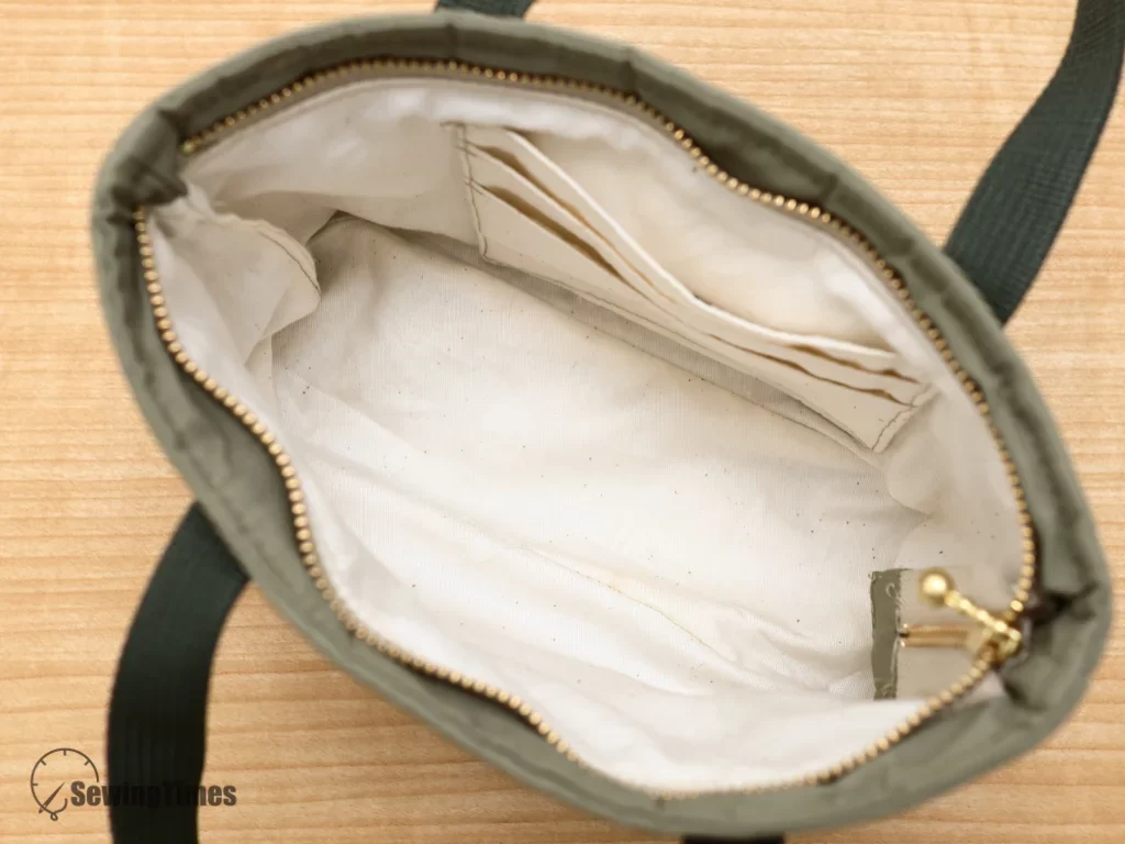 The empty interior of a sewn tote bag displaying a clean cream-colored cotton lining, neatly finished edges, and the integrated card wallet pocket.