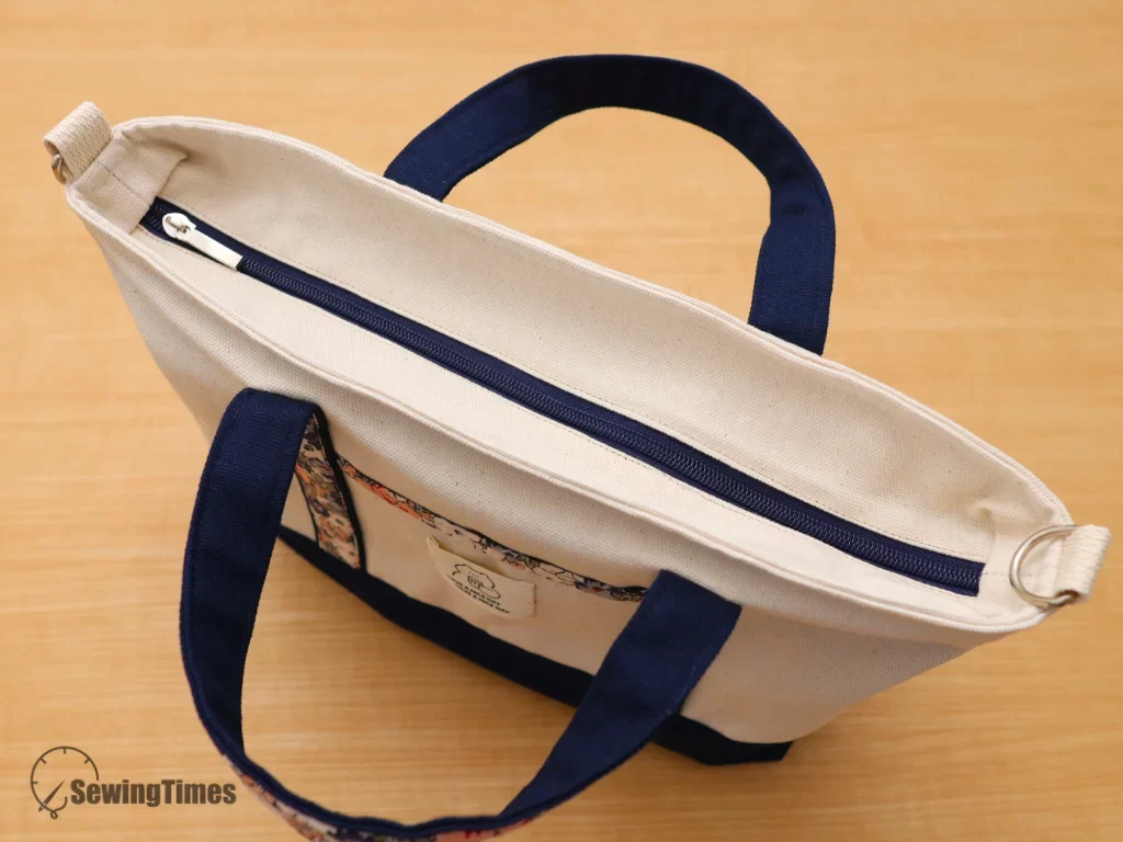 A close-up view of a navy-trimmed canvas tote bag with black sunglasses placed on top, highlighting the detailed floral fabric on the handles.