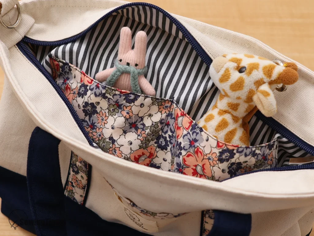 The interior of a handmade tote bag showing a striped lining and multi-pocket organization filled with a small plush rabbit and giraffe toy.