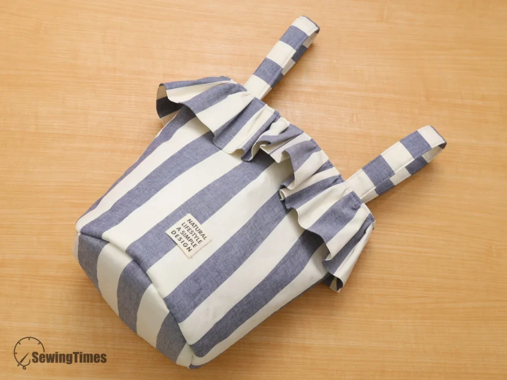Flat-lay view of a stylish handmade ruffle stroller bag on a wooden table, sewing pattern focus.